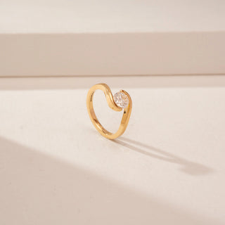 Angled view of a 14KT Yellow Gold diamond ring with a round centre stone and flowing crossover band.