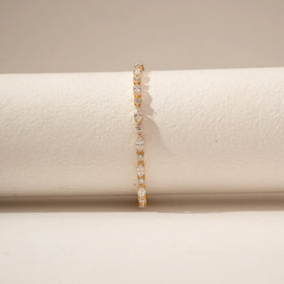 Front view of a diamond tennis bracelet in 14KT Yellow Gold, featuring alternating marquise and round diamonds against a beige backdrop.