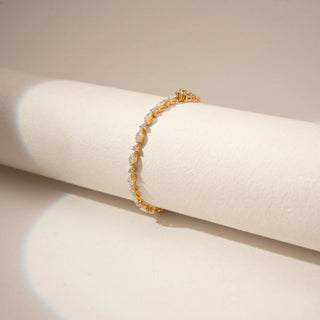 Angled view of a diamond tennis bracelet in 14KT Yellow Gold, featuring alternating marquise and round diamonds against a beige backdrop.