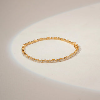 Top view of a diamond tennis bracelet in 14KT Yellow Gold, featuring alternating marquise and round diamonds against a beige backdrop.