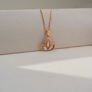 Close-up of a rose gold floral pendant necklace featuring three petal-shaped motifs with sparkling diamond accents, suspended from a delicate chain against a soft cream backdrop.