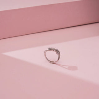 Side view of Reia’s 18 KT White Gold Floral Infinity Diamond Band Ring. Captured against a pink backdrop, it highlights the sleek, contemporary foundation and delicate wave-like silhouette.
