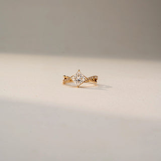 Front view of a princess-cut solitaire engagement ring in 14 KT Yellow Gold, featuring a princess-cut lab-grown diamond set on a twisted pavé diamond band, displayed against a beige backdrop.