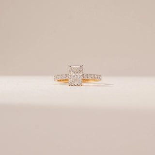 Front view of a radiant diamond ring in 14KT Yellow Gold, featuring a pavé-set band and four-prong centre stone against a beige backdrop.