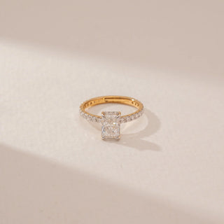 Close-up view of a radiant  diamond ring in 14KT Yellow Gold, featuring a pavé-set band and four-prong centre stone against a beige backdrop.