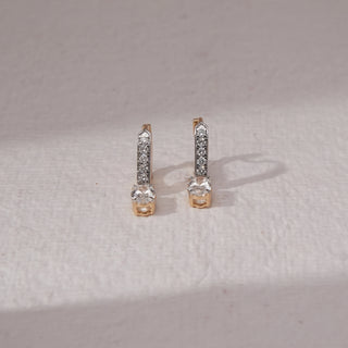 Top view of diamond bar stud earrings in yellow gold, featuring vertical rows of round lab-grown diamonds with a larger round diamond at the base. Set on a soft neutral backdrop, they reflect clean elegance.
