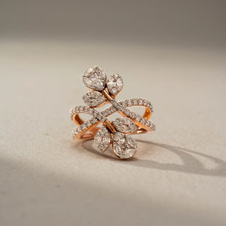 Front view of a floral crossover statement ring in 14 KT Rose Gold, featuring marquise and pear-shaped lab-grown diamonds arranged as blooming leaves on intertwined pavé-set diamond bands, displayed against a beige backdrop.