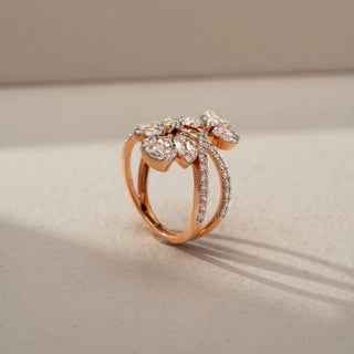 Angled view of a floral crossover statement ring in 14 KT Rose Gold, featuring marquise and pear-shaped lab-grown diamonds arranged as blooming leaves on intertwined pavé-set diamond bands, displayed against a beige backdrop.