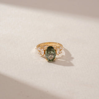 Close-up view of a 14KT Yellow Gold diamond ring featuring an oval green centre stone and sparkling marquise and round diamond accents.