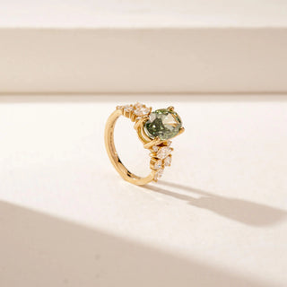 Angled view of a 14KT Yellow Gold diamond ring featuring an oval green centre stone and sparkling marquise and round diamond accents.