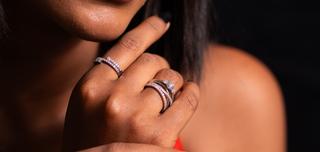 etailed view of a woman’s fingers adorned with stacked Reia lab grown diamond rings in contemporary designs, set against a rich dark background for elegance and contrast.