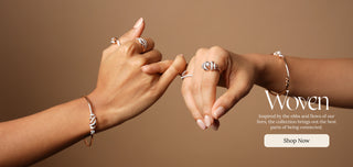 Two hands reaching toward each other, adorned with Reia Lab Grown rings and bracelets, on a warm brown background featuring the ‘Woven’ branding and collection tagline.