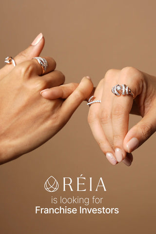 Two hands wearing Reia lab grown diamond rings, touching in a symbolic gesture, with text inviting franchise investors, set against a brown background.