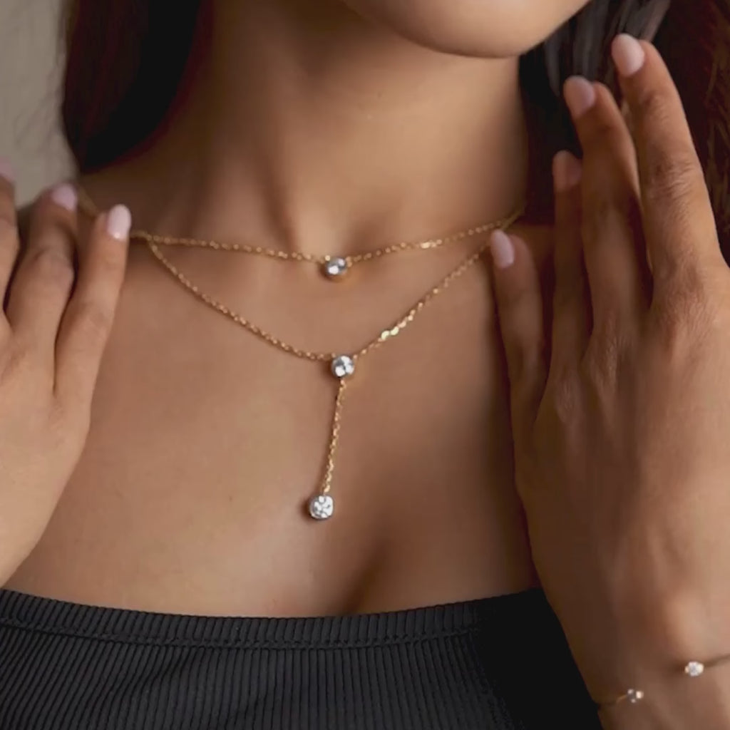 Layered gold necklace worn at the collarbone, featuring bezel-set round-cut lab-grown diamonds on a delicate chain with a vertical drop accent, captured in a front lifestyle close-up against warm skin tones.