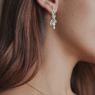  Dangling lab-grown diamond earrings by Réia in 14KT Yellow Gold, featuring vine-inspired curves and clustered diamonds, worn on the ear in soft natural light.